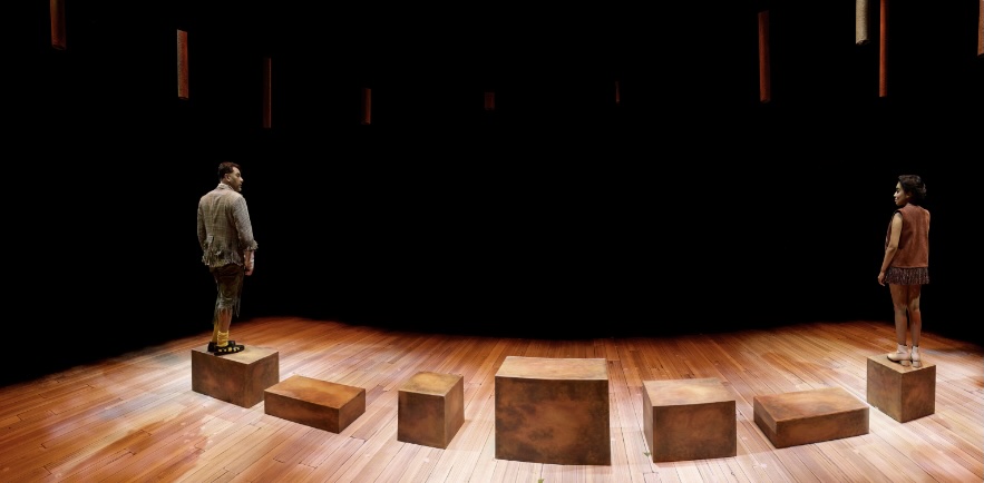 A semicircle of packing crates stretches across the stage, with Peter standing at one end and another character at the opposite end, frozen in theatrical symmetry. Shaw Festival 2025. Photo by Michael Cooper.
