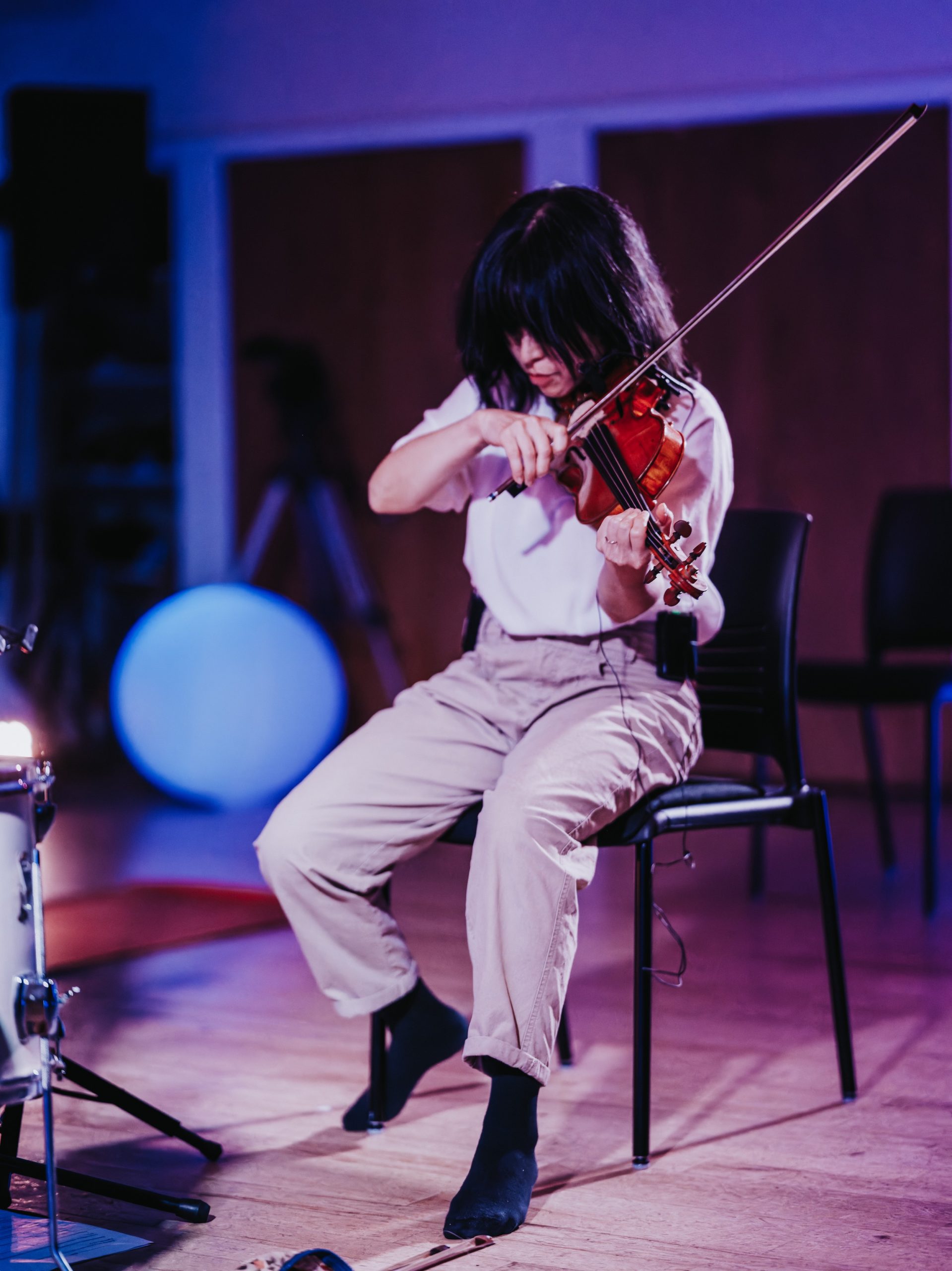 Violinist Leslie Ting plays with passion perched on a chair.