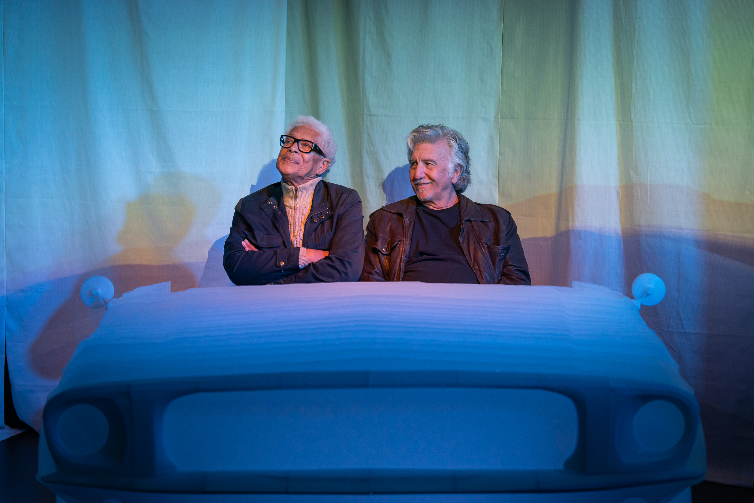 Two characters from An Orchid and other such Lilies and Lies sit together inside a car, captured in a close interior view that highlights their emotional tension.