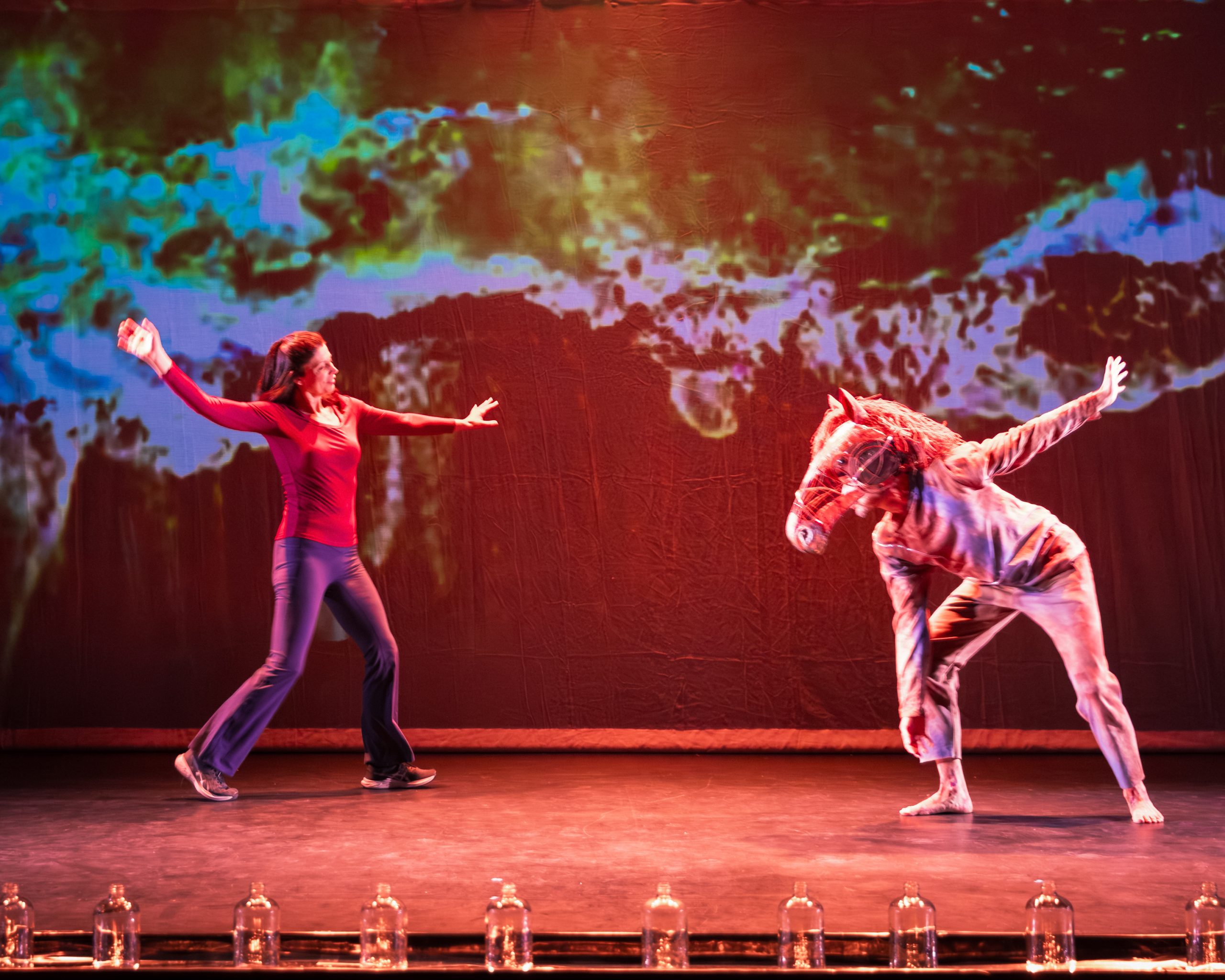 Anita La Selva dancing with the horse empty bottles in the foreground, projections in the background,