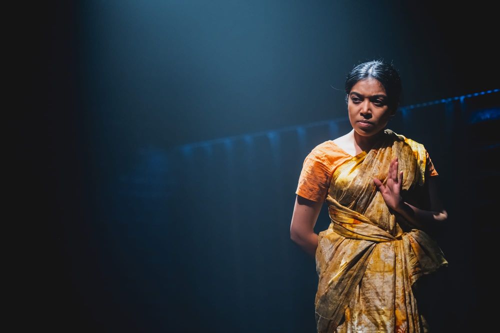 Woman standing quietly but looking intently ahead wearing a sari.