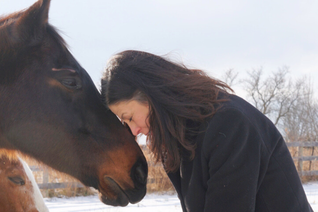 Anita resting her head on the horse's head, her eyes closed.