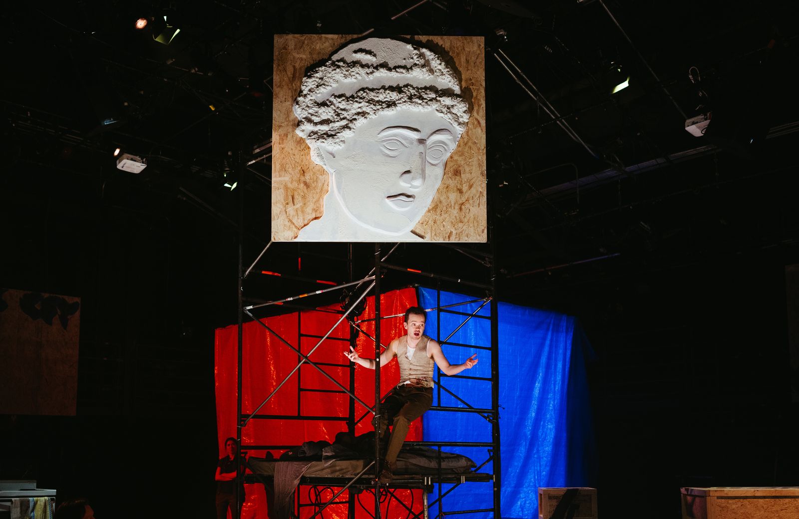 A huge plaster of Sappho above a man sitting in the upper scafolding,