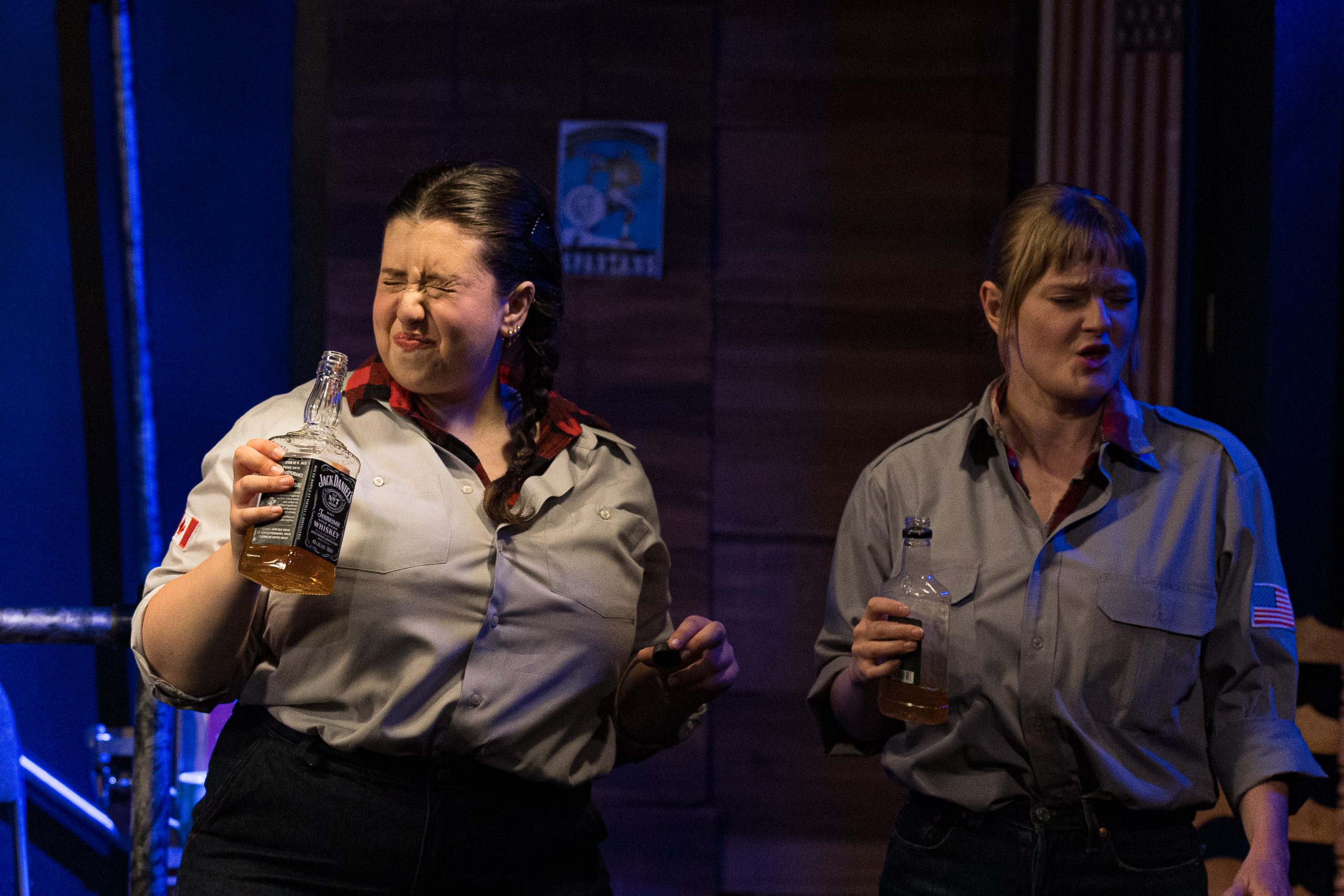 the two sues trying each country's liquor and hating it, holding bottles of boubon and canandian club