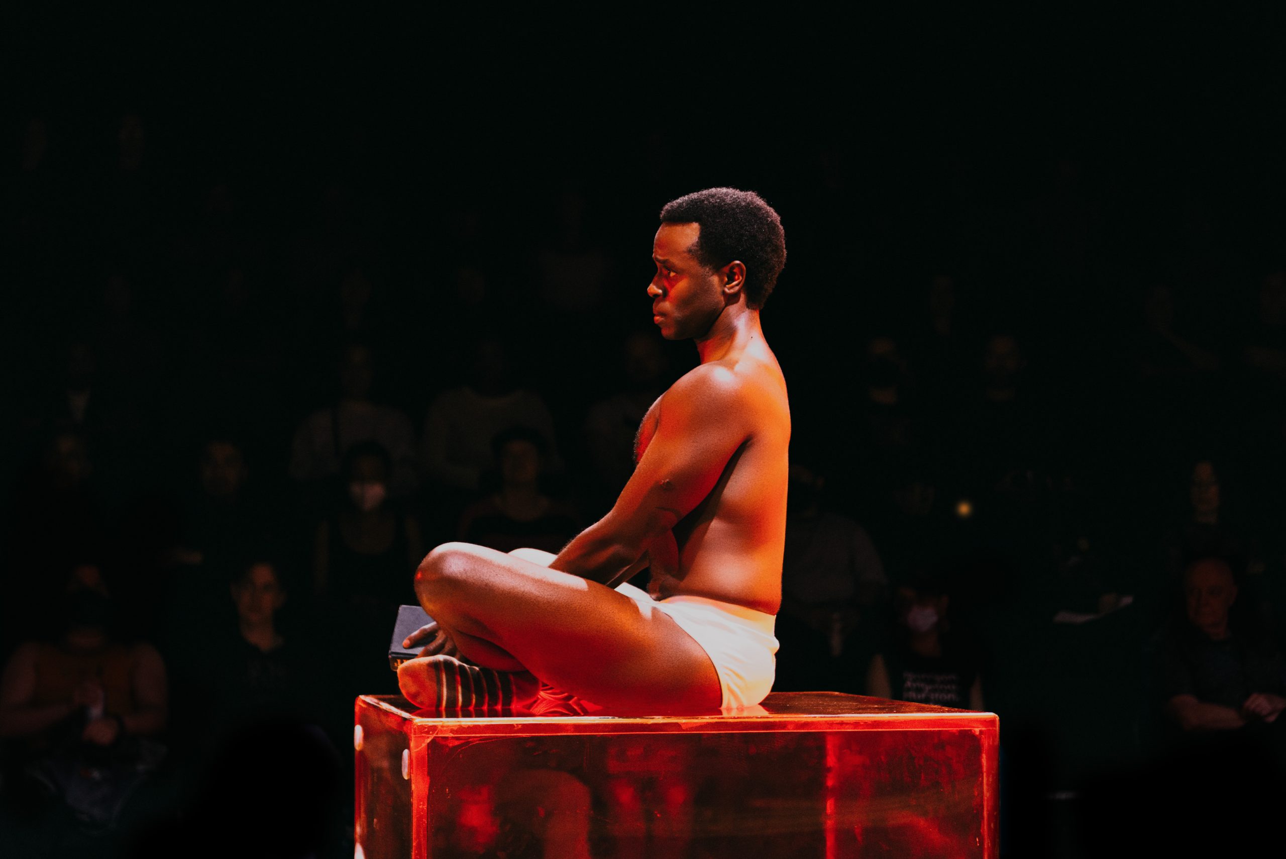 Kyle Brown as baby Sutter sitting cross-legged, facing sideways, wearing just briefs